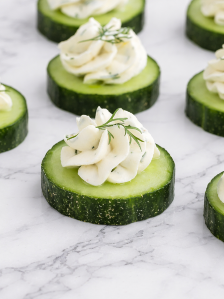 A selection of elegant cucumber cream cheese canapés arranged on a platter, garnished with fresh dill and herbs, ready to serve at a party.