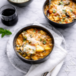 A rustic bowl of Tuscan bread soup (Ribollita) with kale, beans, vegetables and torn bread soaking in a rich broth, garnished with olive oil and herbs.