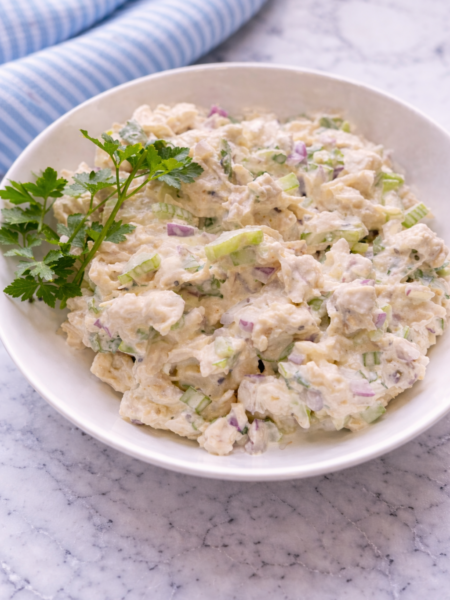A bowl of classic Chicken Salad Chick style chicken salad with diced chicken, celery, juicy grapes, crunchy nuts, and creamy dressing, garnished with herbs and served with crackers.