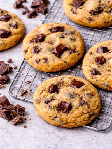 Close-up of homemade golden chocolate chip cookies with soft centers and visible melted chocolate chips on the surface, served on a cooling rack.