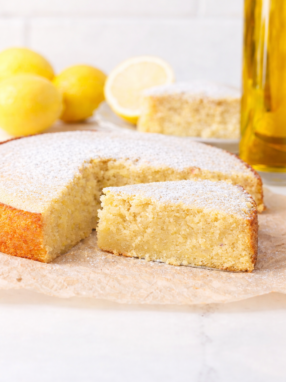 Moist lemon olive oil cake topped with powdered sugar and fresh lemon slices on a rustic plate